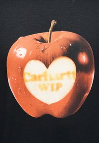Κόκκινο μήλο με σταγόνες νερού και φωτεινή κηλίδα σε σχήμα καρδιάς στο κέντρο, που απεικονίζει θολό κείμενο "Carhartt WIP" σε μαύρο φόντο.