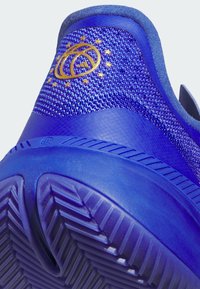 Scarpa atletica blu con tomaia in mesh texturizzato e suola in gomma liscia. Include un accento con emblema dorato sul tallone.