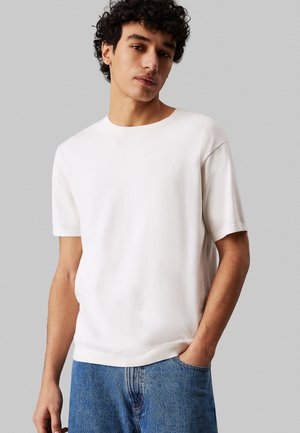 T-shirt bianco a maniche corte con colletto rotondo, realizzato in un morbido tessuto testurizzato. Il design presenta un logo discreto sul petto.