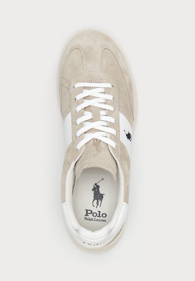 Beige suede sneaker with white leather stripe, white laces, and logo printed on insole. Rounded toe and textured rubber sole.