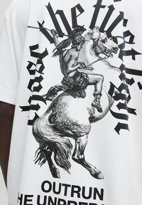 Sort-hvid illustration af en kriger i hjelm, der rider på en oprejst hest, omgivet af stiliseret gotisk tekst på en hvid skjorte.