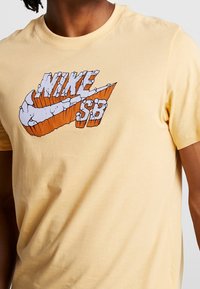 Camiseta de algodón amarilla con un diseño gráfico del logo de Nike en naranja y blanco, con un patrón texturizado y letras en negrita.