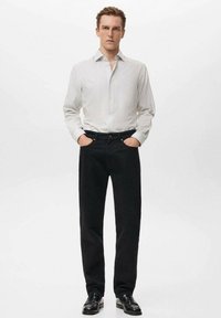 Camisa de botón blanca a rayas con mangas largas, pantalones negros y zapatos negros; ajuste casual con una textura suave y un diseño clásico.