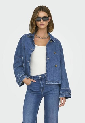 Denimjakke med en cropped design, lyseblå farge, doble knapper og vide ermer. Kombinert med en hvit topp og blå jeans.