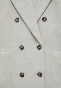 Blazer de corte cruzado en un suave tono gris claro, confeccionado en una tela blanda, con cuatro botones oscuros, dos bolsillos frontales y un diseño de solapa muesca.