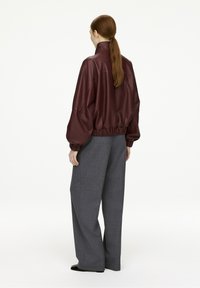 Burgundy leather jacket with a high collar, gathered hem, and oversized sleeves paired with gray wide-leg trousers and black footwear.