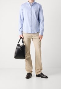 Ljusblå långärmad skjorta med knappar och vit logotyp, beige raka byxor, svarta läderskor och en svart läderhandväska med dragkedja.