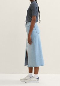 Jeanskjol i ljusblått med en slits framtill, kombinerad med en marinblå och vitrandig kortärmad skjorta samt vita sneakers med grå detaljer.