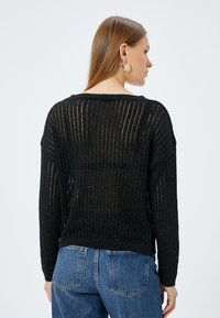 Svart stickad tröja med vertikala randiga mönster, avslappnad passform och långa ärmar. Texturerat, lätt material med en lätt glans.