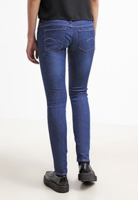 Vaqueros de denim azul ajustados con una textura suave, cintura de media altura y bolsillos traseros con parche. Combinados con zapatos de plataforma perforados negros.