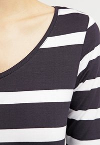 Námořnický pruhovaný top s vodorovnými bílými pruhy, širokým výstřihem do V a měkkou bavlněnou tkaninou, která má těsný střih.