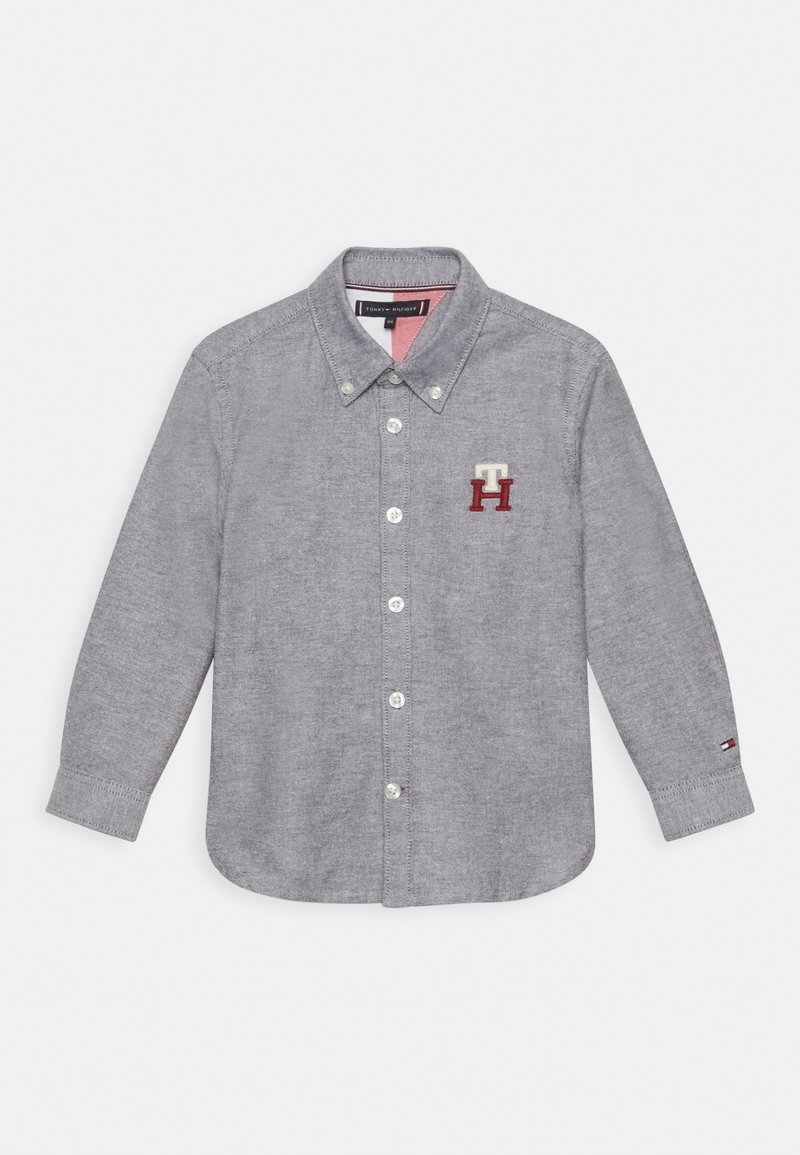 Chemise à manches longues gris avec col et logo "TH" brodé sur la poitrine gauche, et petit drapeau sur le poignet gauche.
