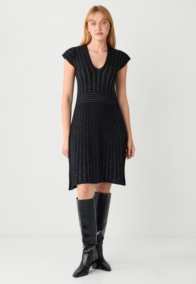 Robe en maille noire avec manches courtes en forme de cape, col en V, rayures verticales texturées, corsage ajusté et jupe évasée ; portée avec des bottes noires montantes jusqu'au genou.