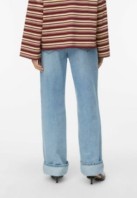 Vaqueros de pierna ancha azul claro con puños remangados y textura desgastada, combinados con un top de manga larga a rayas en granate y beige.