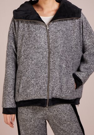 Harmaa vetoketjullinen takki, jossa musta fleecellä vuorattu huppu. Takissa on teksturoitu kangas, sivutaskut sekä mustat resorit hihansuissa ja helmassa.