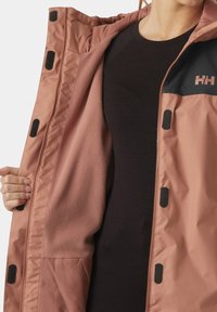 Chaqueta aislante rosa con un panel negro en el hombro, que presenta un interior de forro polar y botones a presión a lo largo de la abertura frontal.