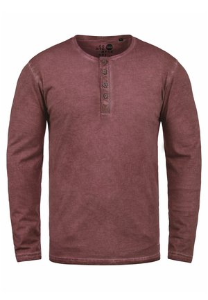 Långärmad, vinröd henley-tröja i mjukt tyg, med rund halsringning och treknappslås, med en något urblekt textur.