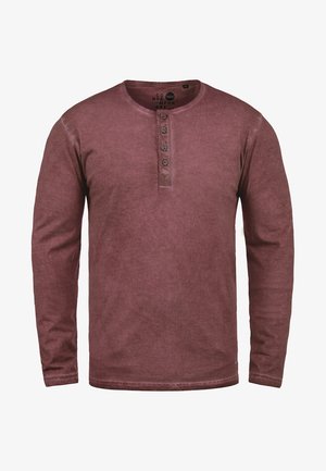 Chemise henley à manches longues de couleur bordeaux, fabriquée en tissu doux, avec un col rond et une patte de boutonnage à trois boutons, affichant une texture légèrement décolorée.