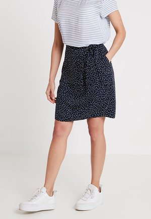 Jupe marine à pois blancs, en tissu léger, taille élastique avec un lien décoratif, associée à un haut rayé gris et blanc et des baskets blanches.