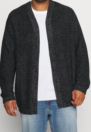 Cardigan negro de punto con un acabado texturizado, de apertura frontal, mangas largas y un corte holgado, usado sobre una camiseta blanca y jeans de mezclilla.
