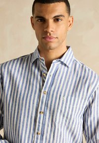 Zila un balta strīpota pogājama krekla ar kabatu, izgatavots no viegla auduma, ar koka pogām un mīkstu tekstūru.