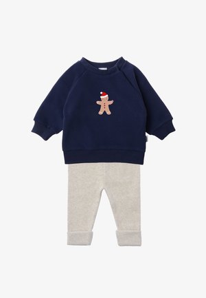Navy blue sweatshirt with a gingerbread man graphic and red accents paired with light gray ribbed pants, featuring cuffed ankles.