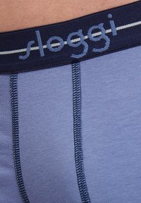 Blå bomullskalsonger med midjeband i marinblått som har den broderade logotypen "sloggi" och kontrasterande sömmar. Mjuk textur och åtsittande design.