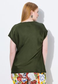 Top de manga corta en verde oliva con una textura suave. El escote es ligeramente redondeado. Se lleva con pantalones multicolores estampados.