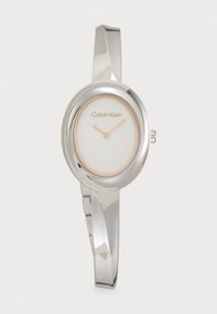 Montre en métal argenté avec un cadran ovale, un fond blanc et des aiguilles minimalistes en ton or. Dotée d'un bracelet de style élégant.