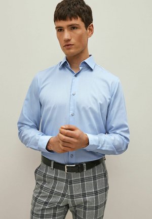 Light blue long-sleeve shirt with a structured collar, flat buttons, paired with gray plaid trousers and a black belt. Smooth texture.