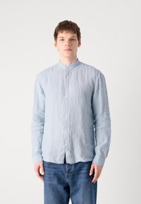 Hellblaues, langärmliges Hemd mit Knopfleiste aus zerknittertem Stoff, mit Mandarin-Kragen und geradem Saum. Kombiniert mit dunklen Jeans.