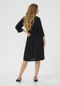 Robe noire avec des manches trois quarts, une taille cintrée et une jupe fluide. Fabriquée en tissu léger, texture lisse, longueur genoux.