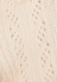 Suéter de punto en beige claro con un delicado patrón de encaje que presenta texturas en relieve y pequeños acentos en forma de puntos a lo largo de la tela.