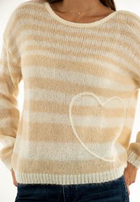 Maglione a righe beige e crema con collo rotondo e maniche lunghe, caratterizzato da un dettaglio a forma di cuore sulla parte anteriore. Tessuto morbido e lavorato.