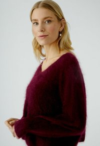 Bordeaux V-hals trui met een fuzzy textuur, lange mouwen en een relaxed fit. Heeft een zachte uitstraling en lichtjes verlaagde schouders.