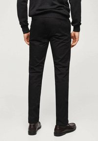 Schwarze Hose mit geradem Bein, gefertigt aus glattem Stoff. Verfügt über zwei Gesäßtaschen und wird mit dunkelbraunen Schuhen getragen.