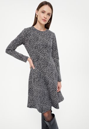 Langärmliges, schwarz-weißes Blumenkleid aus weichem Stoff, mit tailliertem Oberteil und schwingendem Rock. Getragen mit knielangen Stiefeln.