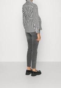 Randig svart-vit långärmad skjorta med bälte i midjan, tillsammans med grå slim-fit byxor och kraftiga svarta skor med nitar.