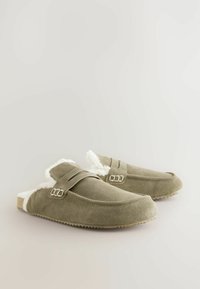 Pantoufles en suede vert olive avec une douce doublure en fourrure blanche, dotées d'une sangle avec deux boucles en métal et d'une semelle en caoutchouc texturée.