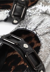 Metaliczne srebrne buty z teksturowanym wykończeniem, czarne paski i metalowe detale. Wnętrze z wzorem w panterkę.