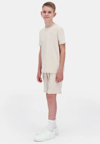 T-shirt beige à manches courtes et short assorti en tissu doux, assortis à des baskets blanches et des chaussettes courtes. Design simple et décontracté.