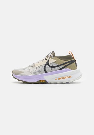 Hellgrauer und olivgrüner Nike ZoomX Laufschuh mit violetter Zwischensohle, schwarzem Swoosh, orangefarbener Lasche und Vibram-Außensohle auf weißem Hintergrund.