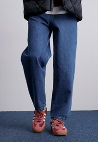 Jeans de mezclilla en un tono azul, con un corte holgado y piernas rectas. Combinados con zapatillas de deporte en color burdeos y blanco.