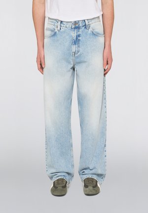 Lyseblå falmede vidde jeans, båret med grønne og brune sneakers og en hvid top, vist fra taljen til fødderne.