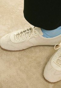 Scarpe in suede beige con finitura liscia, punta tonda e stringhe centrali. Abbinati a calzini alla caviglia azzurri. Suola piatta in gomma.