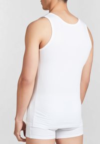 Top in cotone bianco senza maniche con scollatura rotonda, forma aderente e texture liscia, indossato con mutande bianche, visto da dietro.