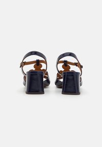 Marine lakk lær block-hæle sandaler med en ankelrem, med utskjærte detaljer og en brun såle. Jevn tekstur og strukturert design.