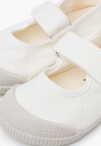 Białe płócienne buty z okrągłym noskiem, z teksturowaną gumową podeszwą i paskiem na rzep na górze dla bezpiecznego zapięcia.