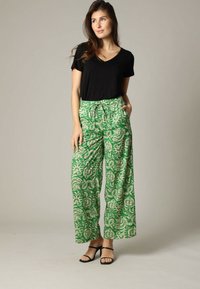 Zwart T-shirt met korte mouwen, gecombineerd met groene wijde broek met een bloemenpatroon in beige. De broek heeft een koordtaille en zakken.