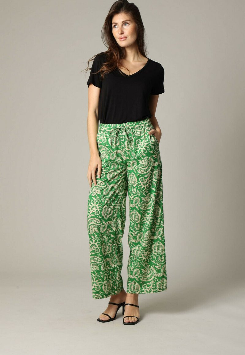 Zwart T-shirt met korte mouwen, gecombineerd met groene wijde broek met een bloemenpatroon in beige. De broek heeft een koordtaille en zakken.